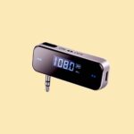 FM transmitter. Audio jack connection, an on off slide switch and frequency adjustment buttons are visible. as is an lcd screen displaying the current frequency range in MHz and the battery level